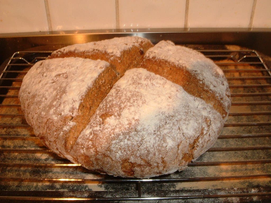 A round loaf of soda bread with a deep cross cut into the top, cooling on a wire rack