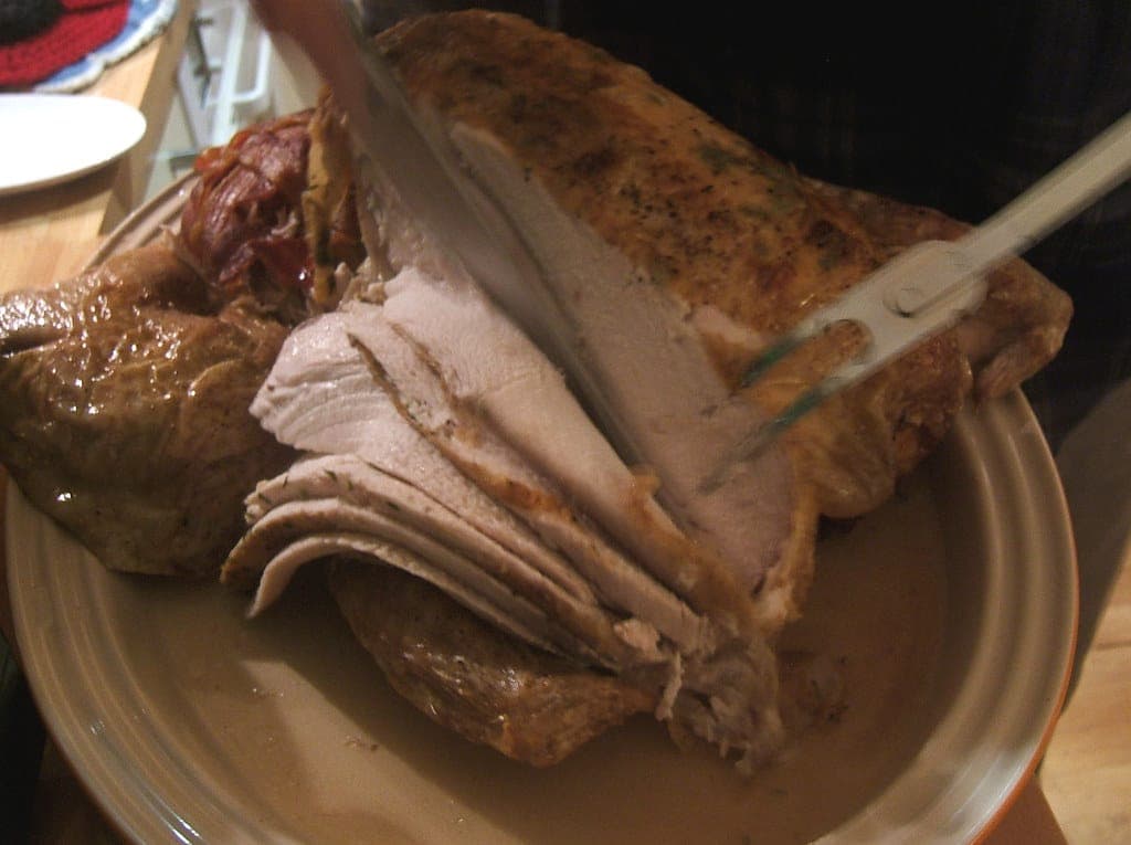 A carving knife and fork slicing breast meat from a roast bird on a platter