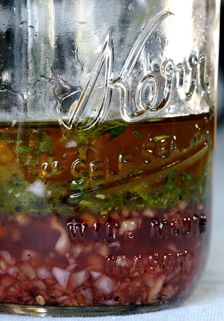 A glass mason jar of herb vinaigrette with olive oil and chopped green herbs