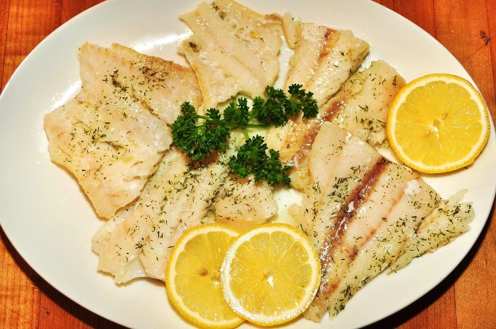 Baked white fish fillets with parsley and lemon slices on a white plate