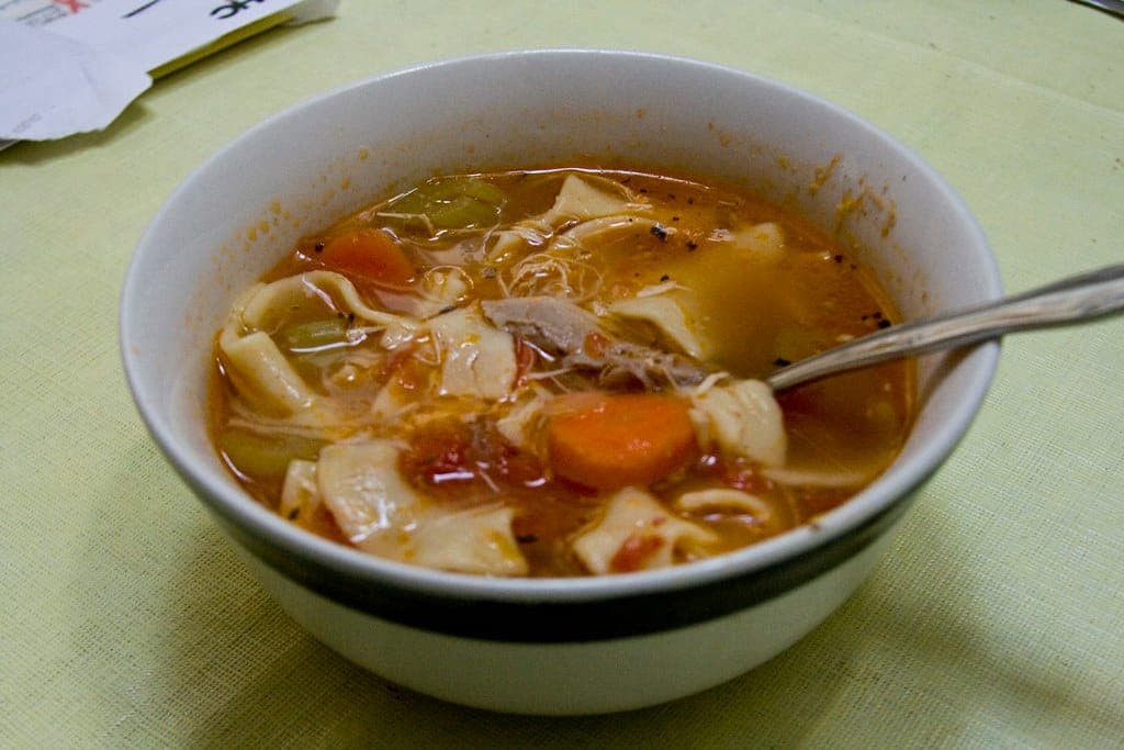 A bowl of chicken noodle soup with carrots, celery and pieces of chicken