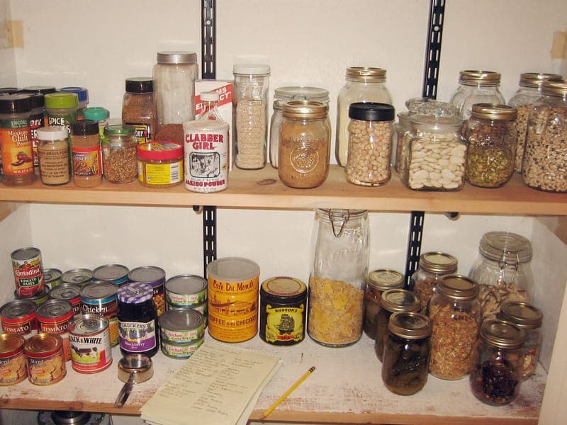 Pantry shelves lined with glass jars of grains, beans and spices alongside canned goods