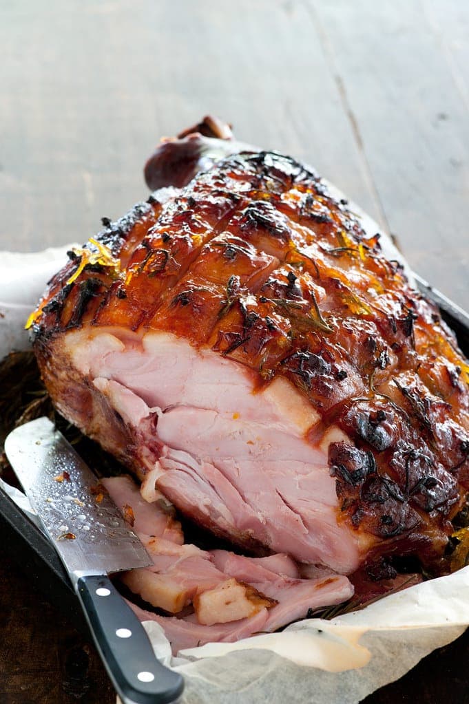 Glossy glazed baked ham, partly carved, with a carving knife on parchment