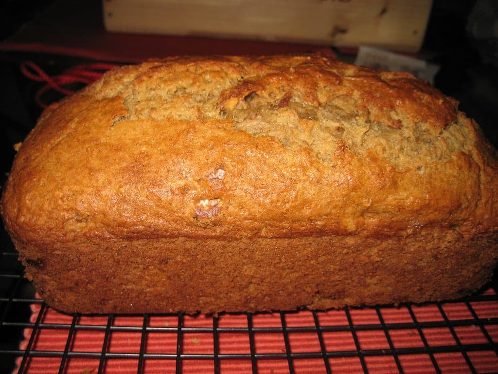 A tall, domed loaf of banana bread cooling on a wire rack