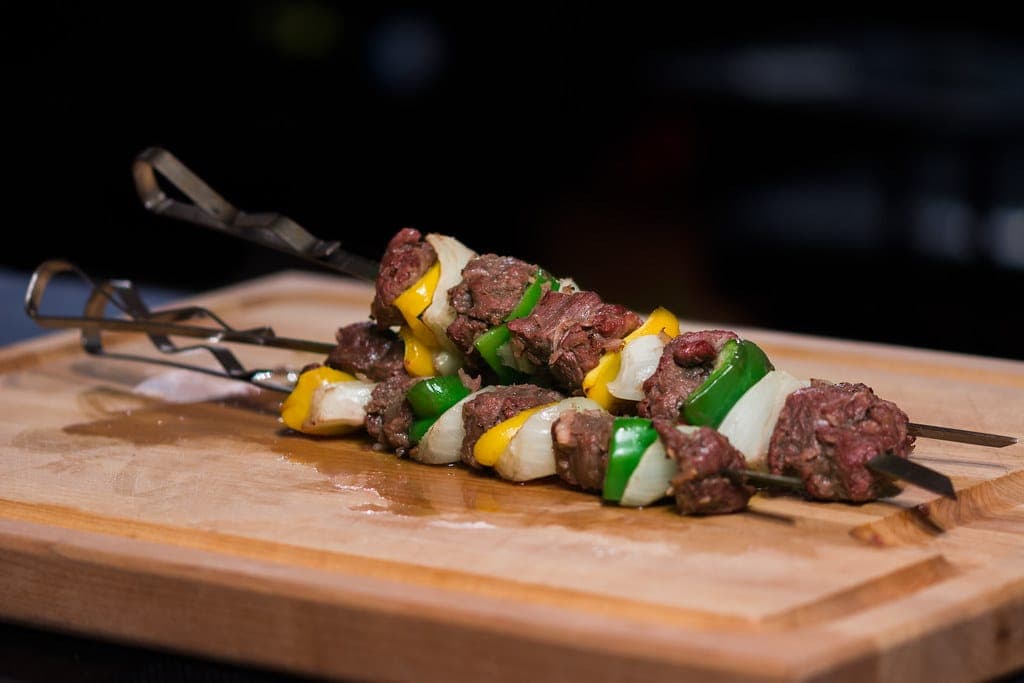 Grilled beef kebabs threaded with green and yellow peppers and onion on a wooden board