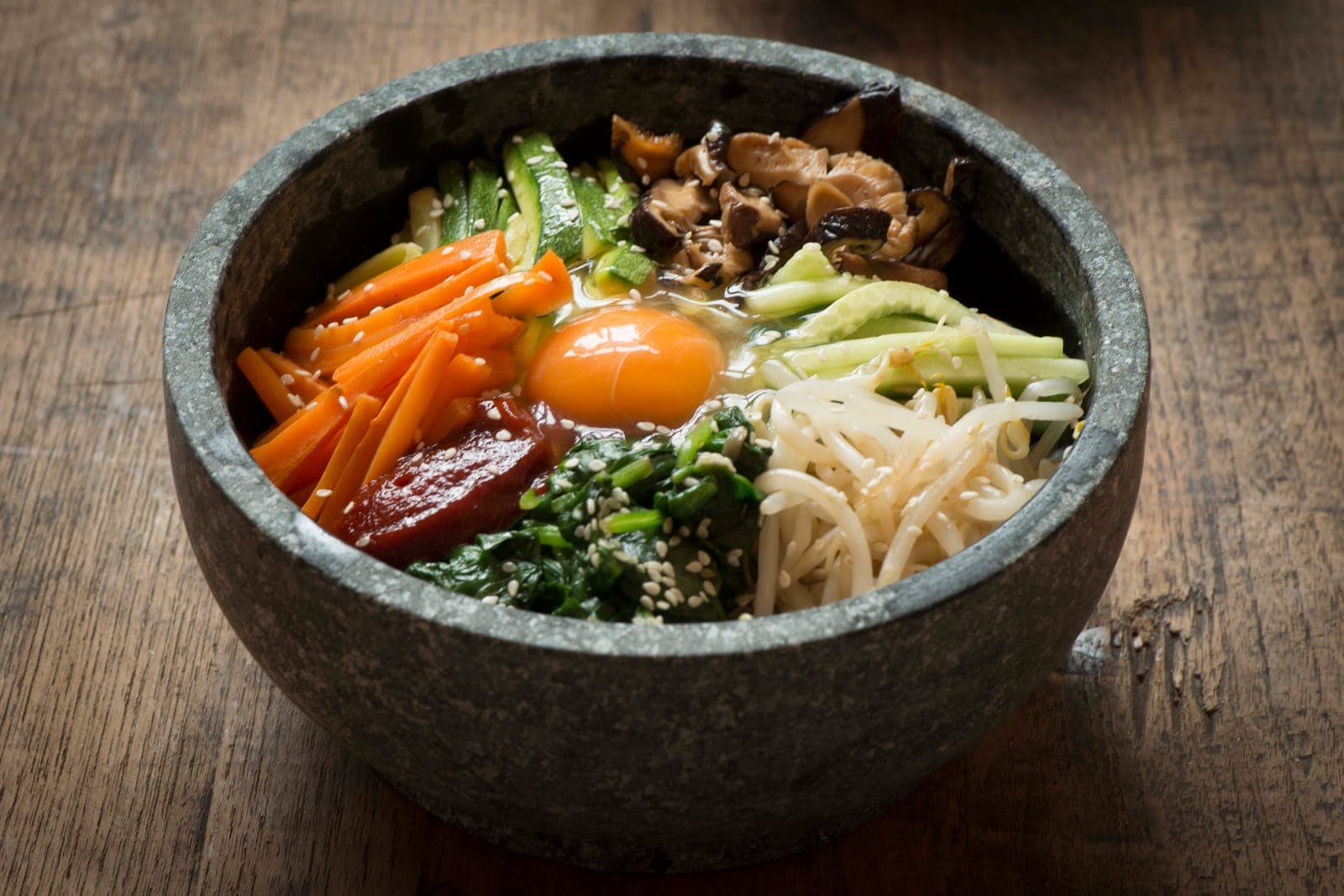 Bibimbap in a stone bowl with an egg yolk, carrots, spinach, bean sprouts, mushrooms and zucchini