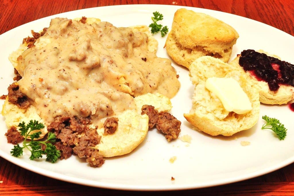 Split biscuits covered in creamy sausage gravy beside a biscuit with jam