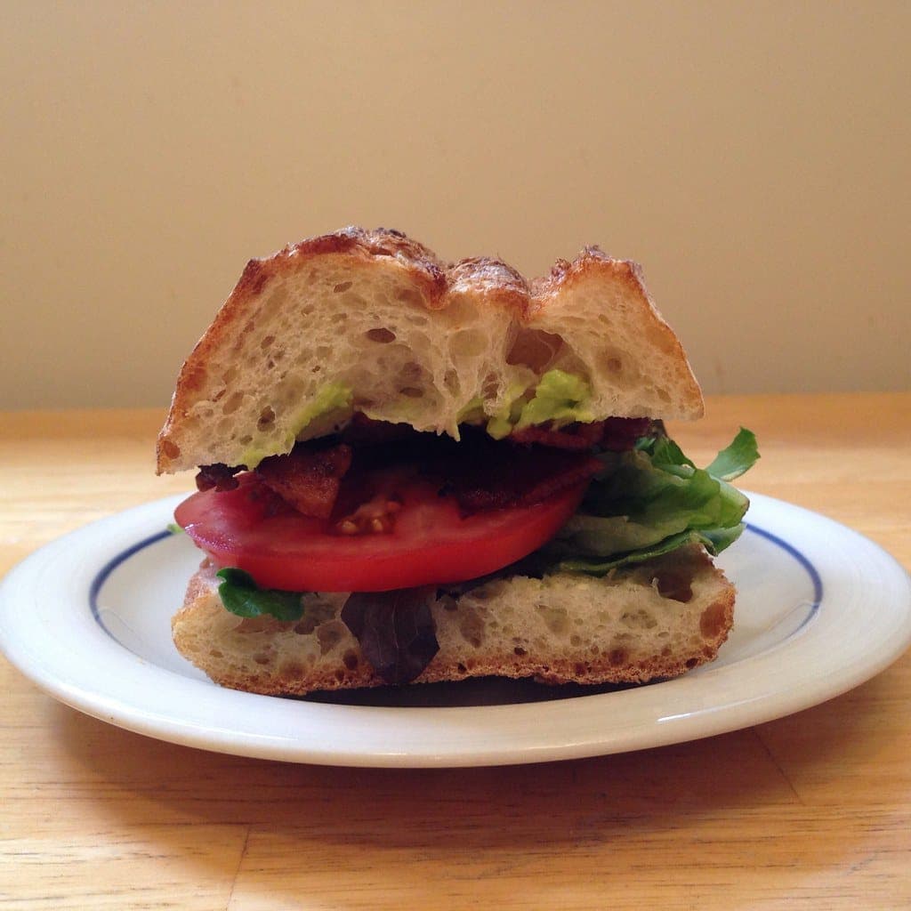 BLT on rustic bread with crisp bacon, a thick tomato slice, lettuce and avocado on a small plate