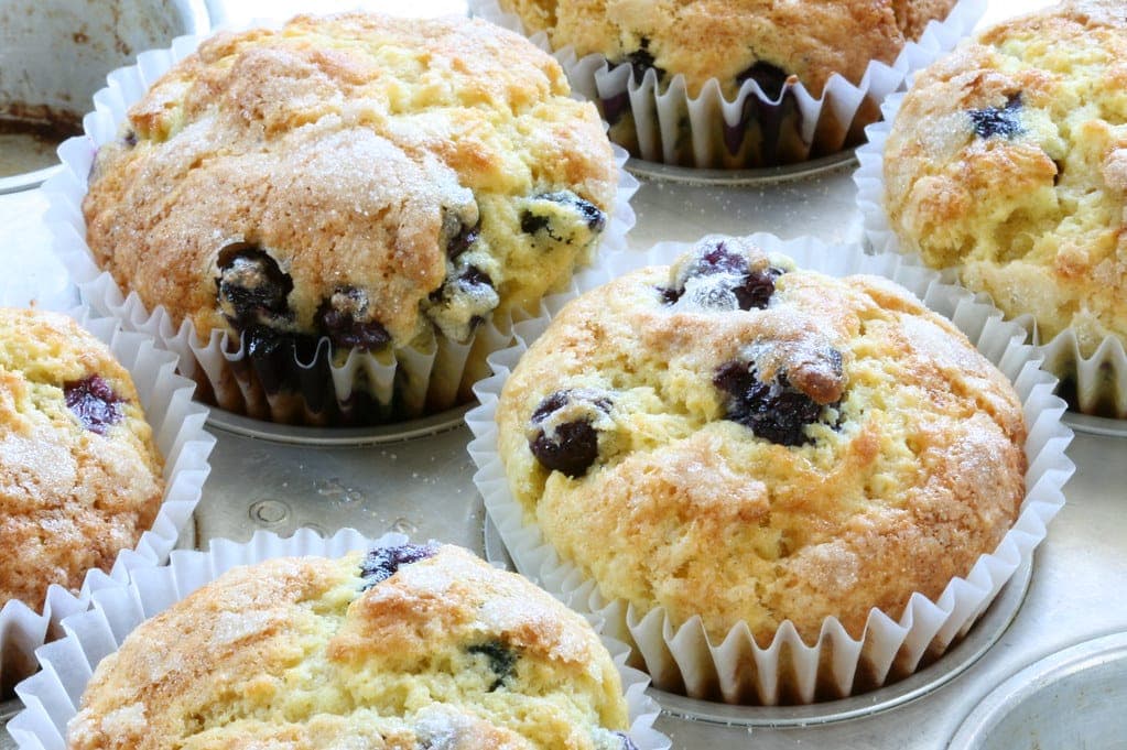 Blueberry muffins with sugar-topped domes in paper liners