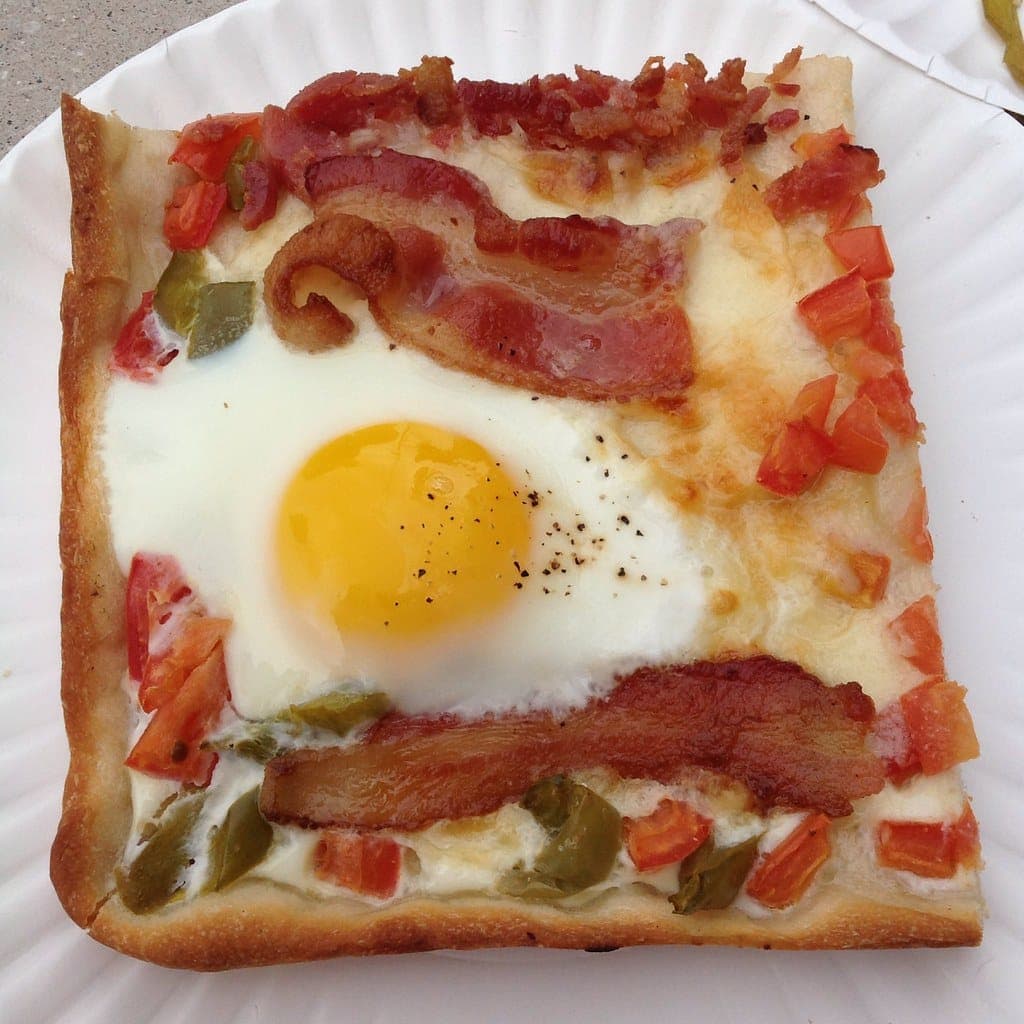 A breakfast pizza topped with bacon, fried eggs and peppers