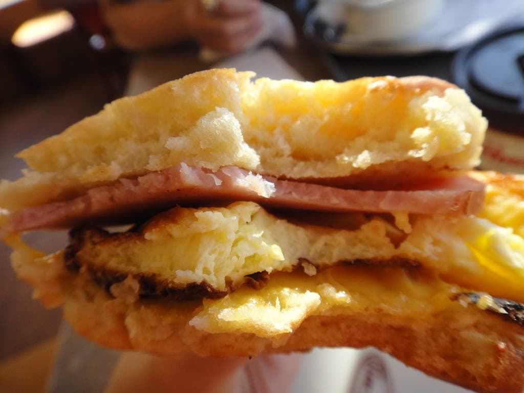 A close-up of a breakfast sandwich with ham, folded egg and melted cheese on a toasted bun