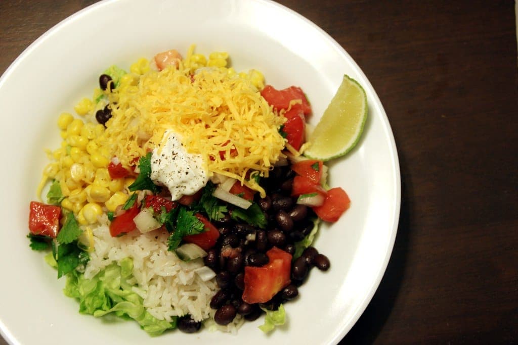 Burrito bowl of rice, black beans, corn, pico de gallo, shredded cheddar, sour cream and a lime wedge