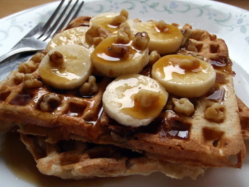Waffles topped with sliced banana, walnuts and syrup on a plate