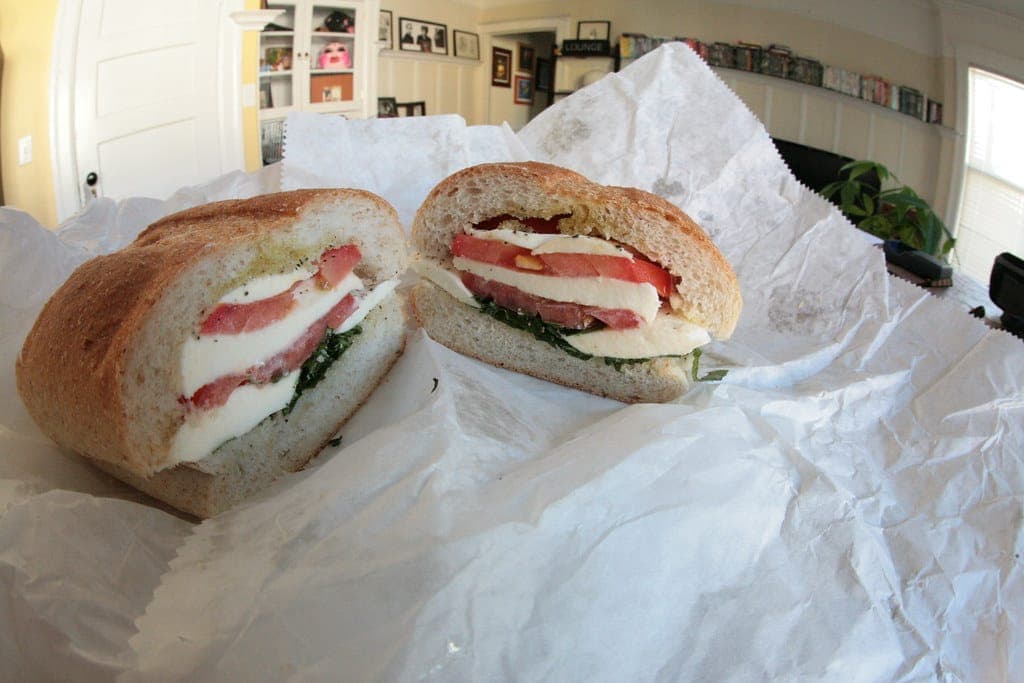 Caprese sandwich cut in half, layered with fresh mozzarella, tomato and greens, on white deli paper