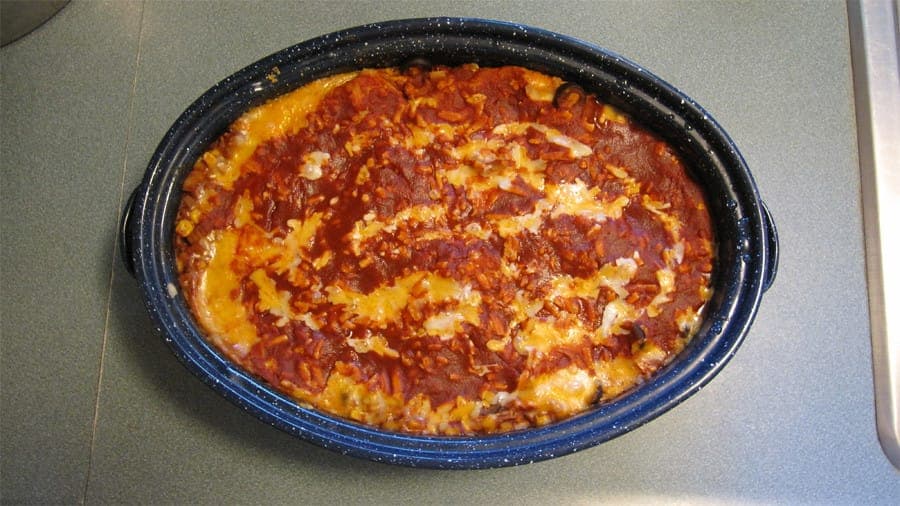 Oval enamel dish of baked enchiladas covered in red chile sauce and melted cheese