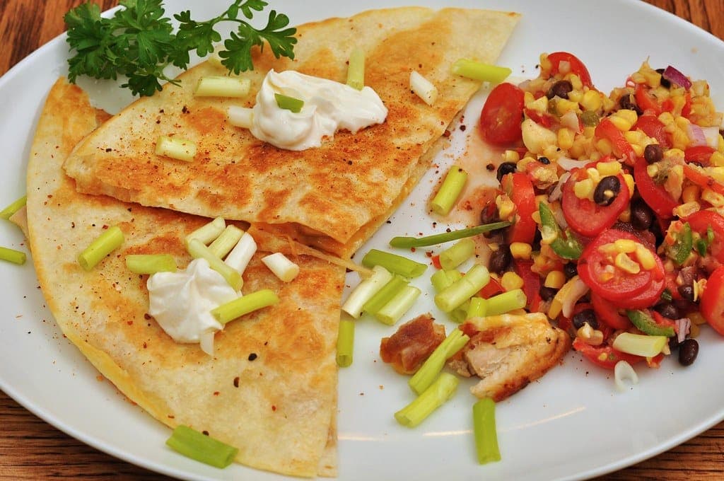 Golden quesadilla wedges topped with sour cream and scallions beside a black bean, corn and tomato salsa