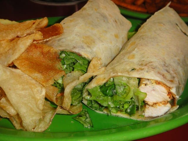 Chicken Caesar wrap cut in half to show grilled chicken and romaine, with potato chips