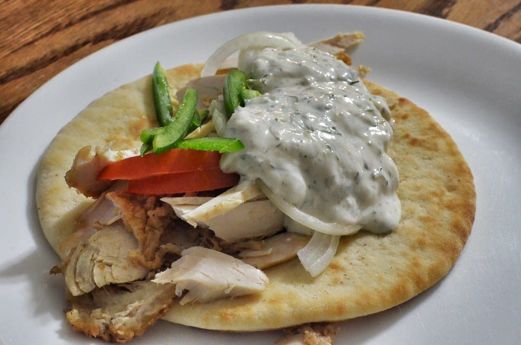 Open pita topped with sliced chicken, tomato, green pepper, onion and a spoonful of tzatziki