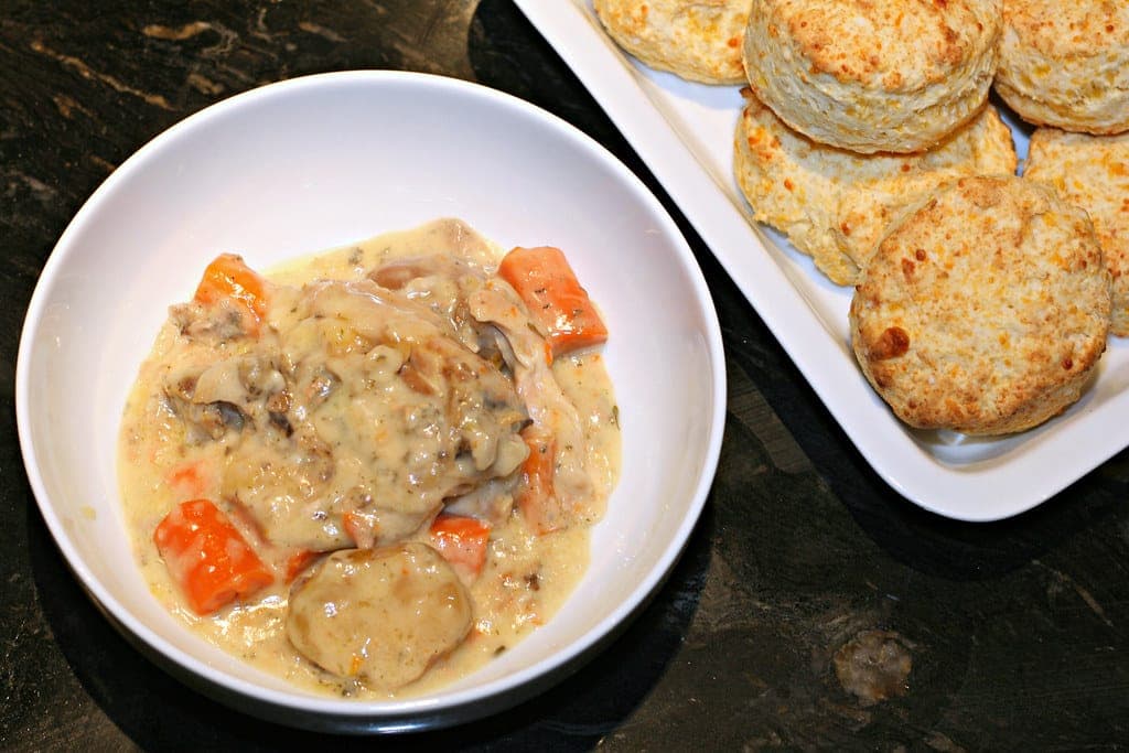 Bowl of creamy chicken stew with carrots and mushrooms beside a plate of biscuits
