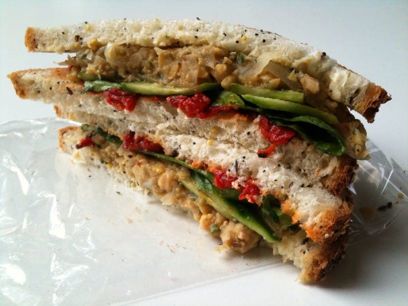 Stacked smashed chickpea salad sandwich with spinach and roasted red pepper on seeded bread
