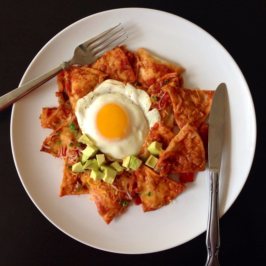 Red chilaquiles topped with a fried egg, crumbled cheese and diced avocado