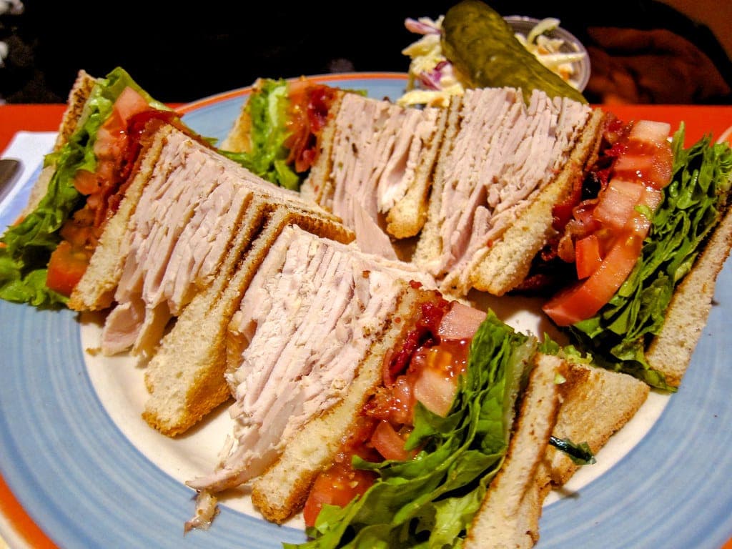 Club sandwich quarters stacked with sliced turkey, bacon, tomato and lettuce on toast, with a pickle