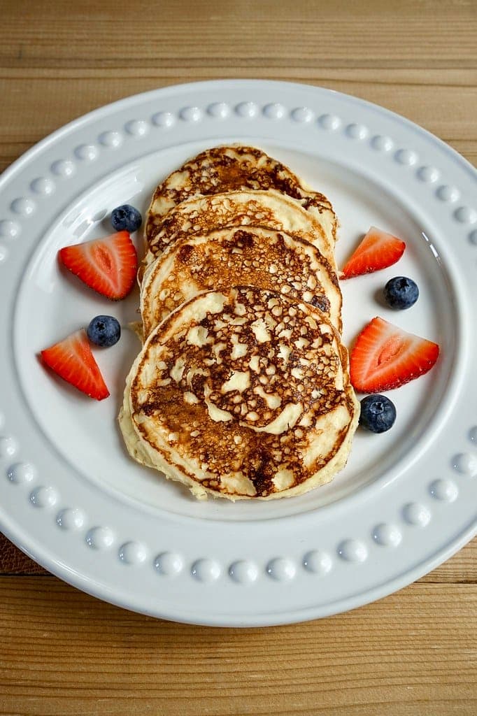 A stack of golden pancakes surrounded by strawberries and blueberries on a white plate