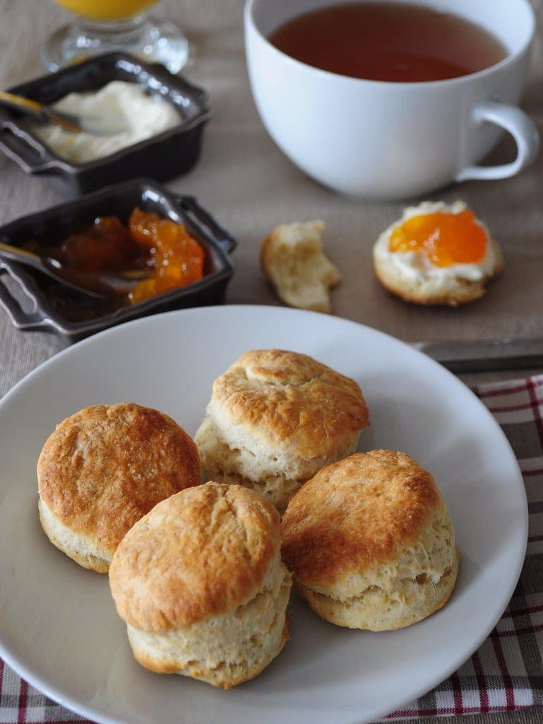 A plate of golden scones with jam and butter in the background