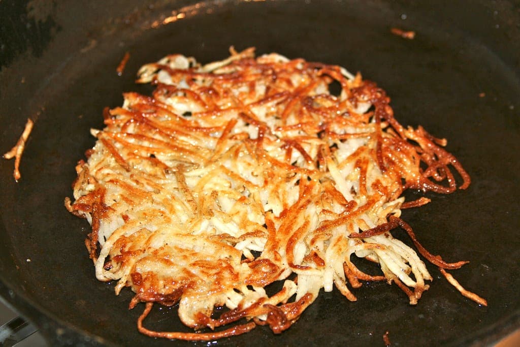 A golden, crispy shredded hash brown cooking in a cast-iron skillet