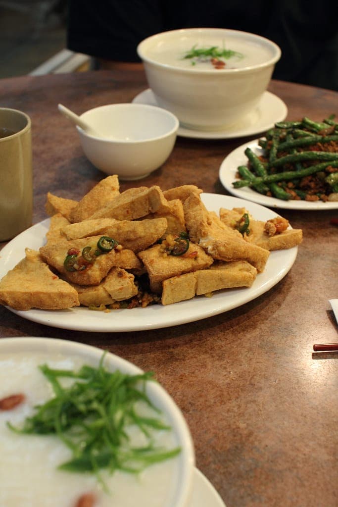 Plate of golden fried tofu triangles with chillies, beside green beans and congee