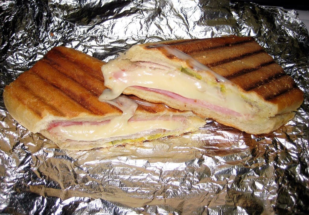 Pressed Cuban sandwich cut open to show ham and melted Swiss cheese, on a sheet of foil