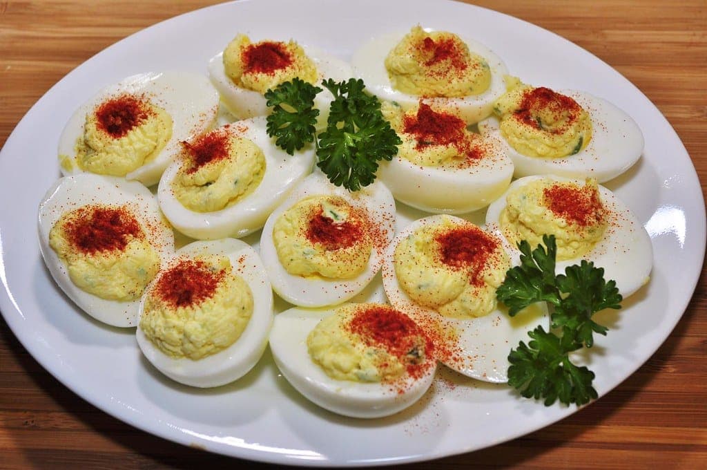 A plate of deviled eggs with piped yellow filling, dusted with paprika and garnished with parsley