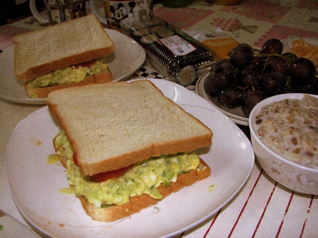 Egg salad sandwiches on soft white bread on a table set for lunch