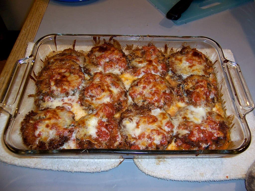 Glass baking dish of eggplant parmesan with browned, bubbling mozzarella and tomato sauce