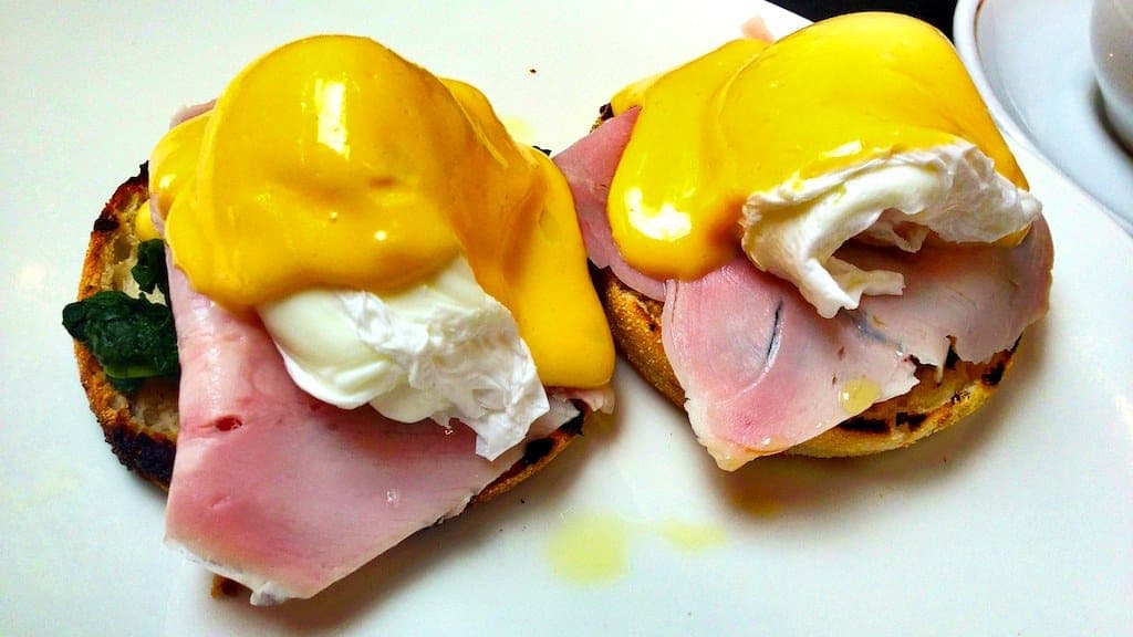 Two eggs Benedict with ham and bright yellow hollandaise on English muffins