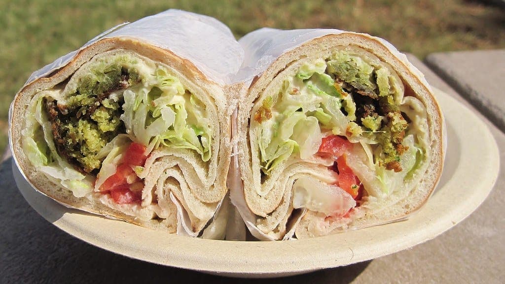 Falafel wrap cut in half to show falafel, lettuce, tomato and sauce, on a paper plate