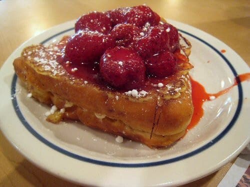 Thick French toast topped with raspberries and powdered sugar on a white plate