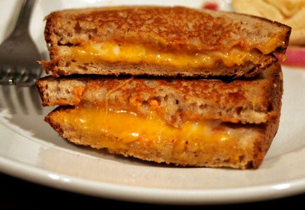 Grilled cheese sandwich halves stacked on a plate, oozing melted orange cheddar