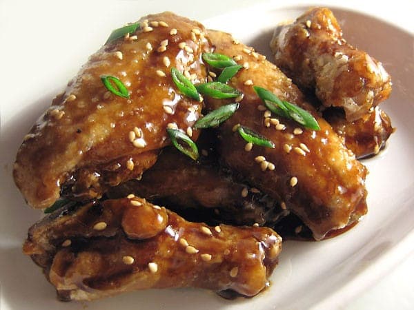Glossy, sticky glazed chicken wings sprinkled with sesame seeds and sliced scallions on a white plate