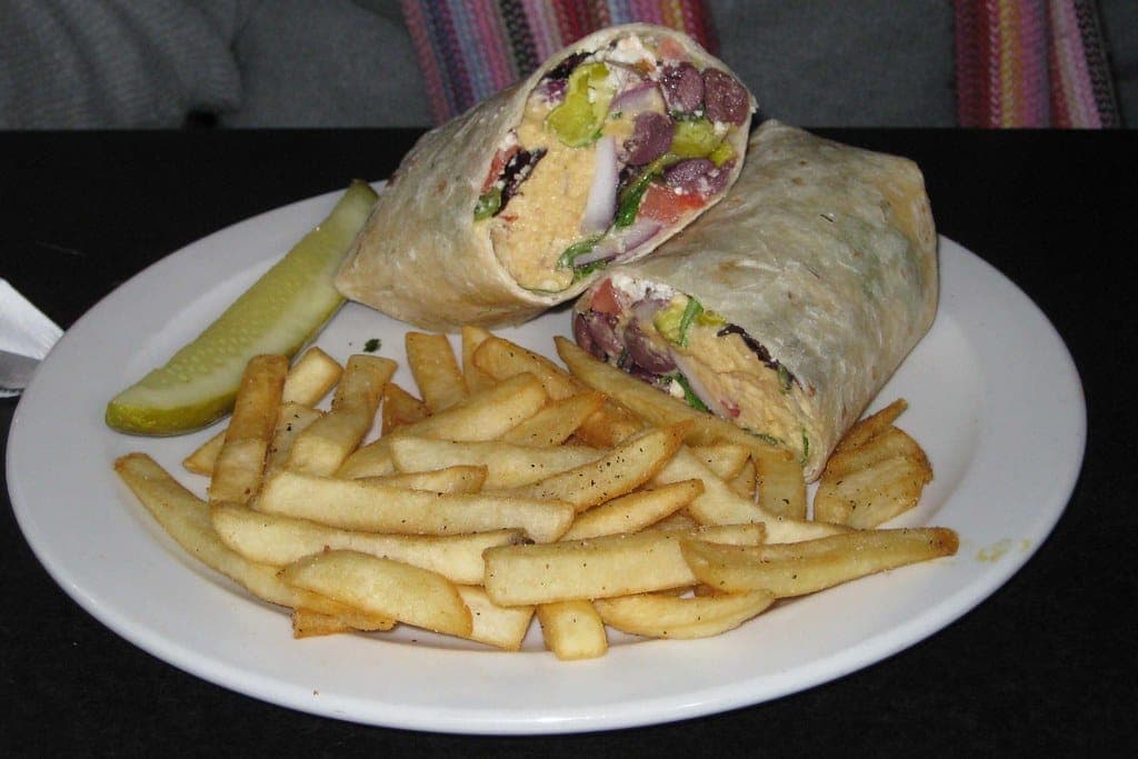 Hummus and vegetable wrap cut in half, served with fries and a pickle spear