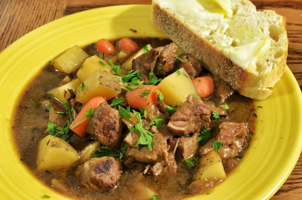 Irish stew of lamb, potatoes and carrots in gravy on a yellow plate with buttered bread