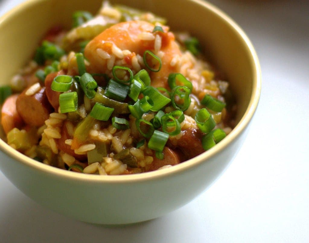 Bowl of jambalaya with rice, sausage, shrimp and celery topped with sliced scallions