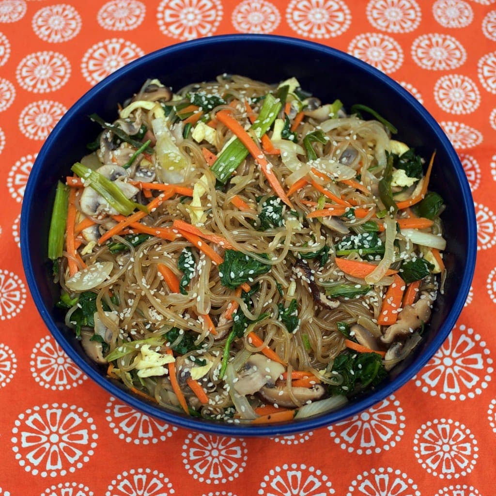 Bowl of japchae glass noodles with spinach, carrot, mushrooms, egg strips and sesame seeds