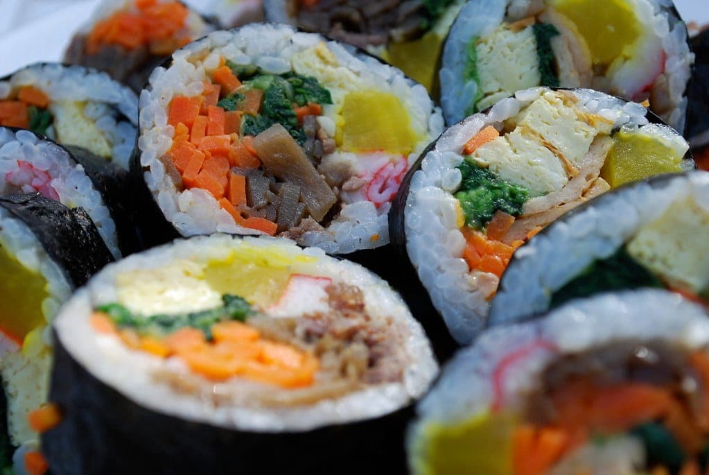 Close-up of sliced kimbap rolls showing rice, egg, carrot, spinach, pickled radish and imitation crab
