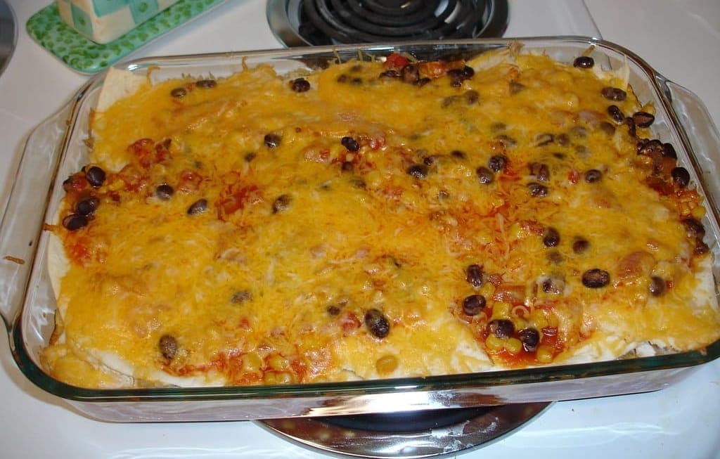 Glass baking dish of layered tortilla casserole topped with melted cheddar, black beans and corn