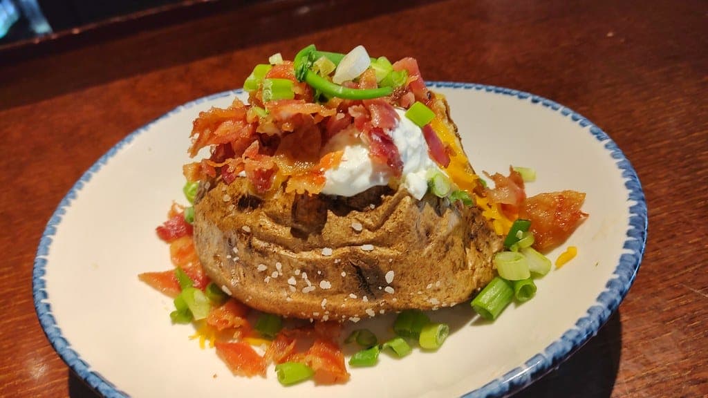 Loaded baked potato topped with sour cream, bacon, cheese, tomato and scallions