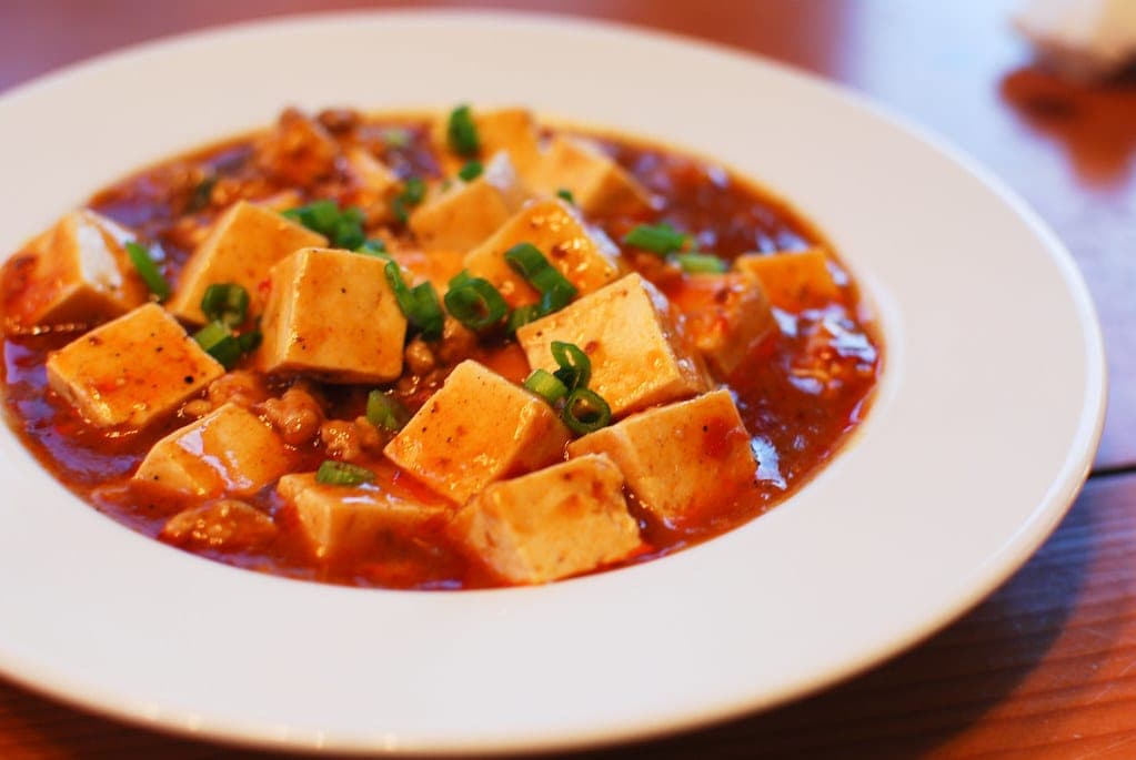 Mapo tofu: cubes of tofu in a glossy red chilli sauce with scallions in a white bowl