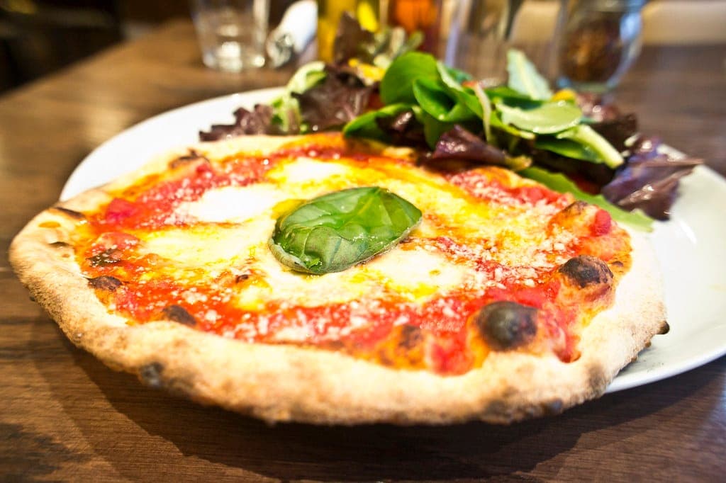Margherita pizza with a blistered crust, tomato, melted mozzarella and a basil leaf, with salad