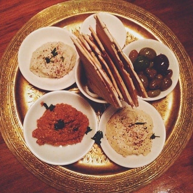 Mezze plate with hummus, a red pepper dip, a second creamy dip, olives and crisp flatbread