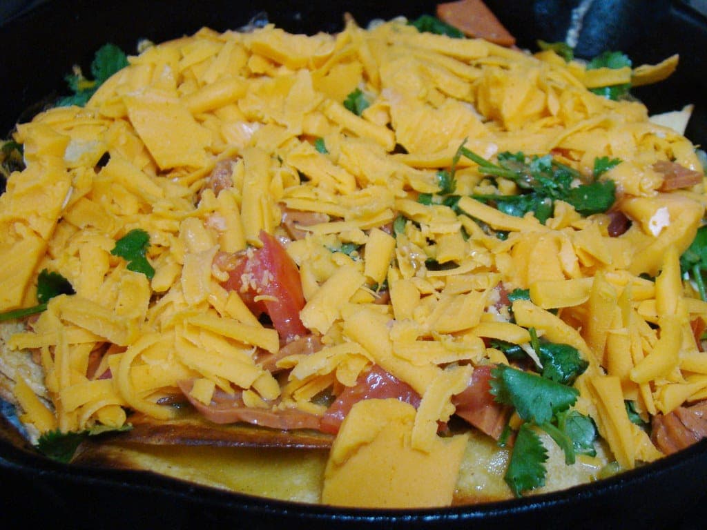 A cast-iron skillet of migas topped with shredded cheddar, tomato and cilantro